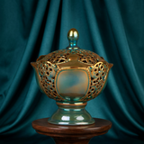Decorative pierced Eosin bonbonier on a wooden stand against a teal curtain background