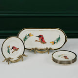 Set of decorative ceramic plates with bird designs on a white surface against a dark green background.