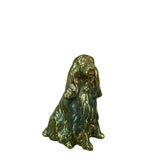 A small figurine of a long-eared dog, an English Cocker Spaniel, with a glossy metallic Eosin finish in olive green and gold tones, set against a plain white background.