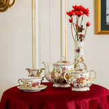 Decorative tea set on a red tablecloth with a vase of red flowers and wall sconce in a stylish room.