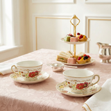 Tea set with floral design on a tablecloth, accompanied by a three-tiered stand with pastries.