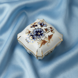 Decorative ceramic box with floral patterns on a blue fabric background