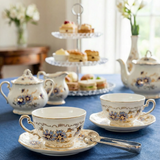 Tea set with floral patterns on a blue tablecloth, accompanied by pastries and a teapot.