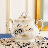 Decorative white sugar bowl with floral patterns on a lace tablecloth.