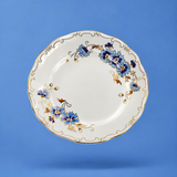 A white ceramic plate with blue floral patterns and gold accents, shown floating against a solid blue background.