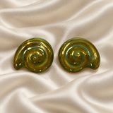 A pair of oval spiral-shaped earrings with a glossy green eosin finish, displayed on a draped cream satin fabric background.