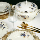 Elegant table setting with floral-patterned dishes, gold cutlery, and glassware on a white tablecloth.