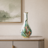 A tall, narrow porcelainvase with a white base and a colorful tropical leaf pattern in green, blue, orange, and red, displayed on a light gray console table against a beige wall.