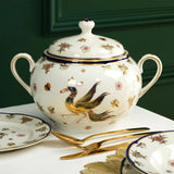 Decorative teapot with phoenix design on a white surface against a green background