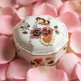 Hand-painted Zsolnay Butterfly porcelain octagonal bonbonniere with lid, decorated with pink and yellow floral motifs and gold accents, resting on pink rose petals.