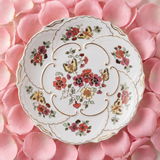 Large hand-painted Zsolnay Butterfly porcelain wall plate featuring pink and yellow floral motifs, butterflies, and a gold scalloped border, resting on pink rose petals.
