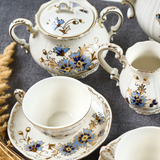 Close-up view of the Zsolnay Cornflower porcelain coffee set showing a sugar bowl, creamer, and a cup on a saucer, featuring hand-painted blue flowers and 18K gold borders.