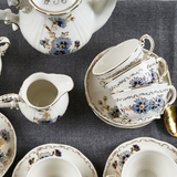 Top-down view of the Zsolnay Cornflower porcelain coffee set featuring stacked cups, saucers, a creamer, and a coffee pot with hand-painted blue flowers and 18K gold borders.